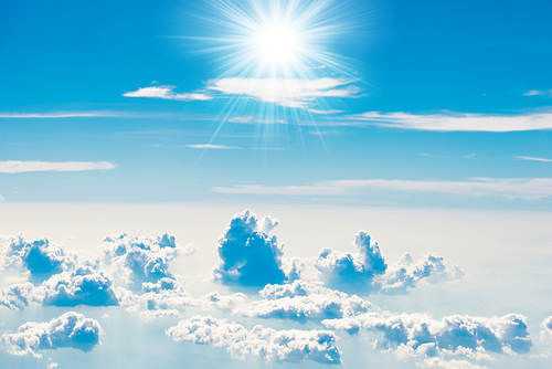 Blue sky with white clouds and shining sun rays, above aerial view from a plane, nature blue sky background