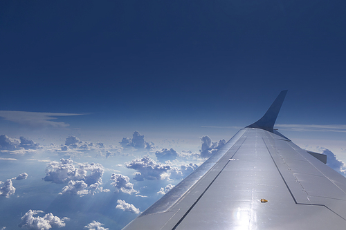 View from the window of airplane on an aircraft wing on a background of blue cloudy sky in a sunny day. Place for your text. Travel and transportation concept.