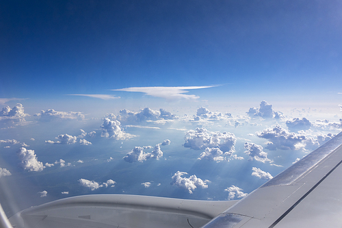 Aiplane window view to the wing of aircraft on a background of clean blue sky with white cumulus clouds, place for text. Travel and transportation concept.