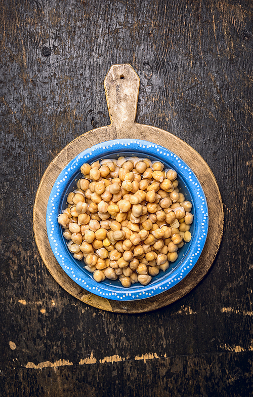 Chick peas, hummus in blue bowl with water on rustic wooden background, top view
