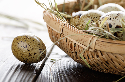 Fresh organic quail eggs in small wicker basket on rustic kitchen table. Space for text