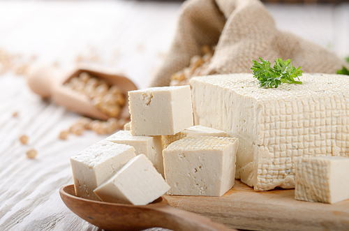 Soy Bean curd tofu on cutting board and in hemp sack on white wooden kitchen table. Space for text