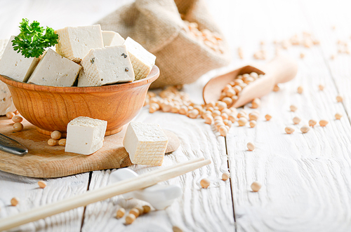 Soy Bean curd tofu in wooden bowl and in hemp sack on white wooden kitchen table. Non-dairy alternative substitute for cheese. Place for text