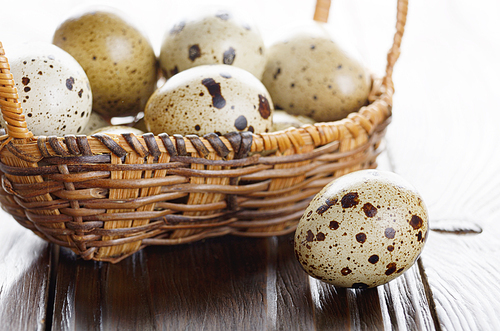 Fresh organic quail eggs in small wicker basket on rustic kitchen table. Space for text