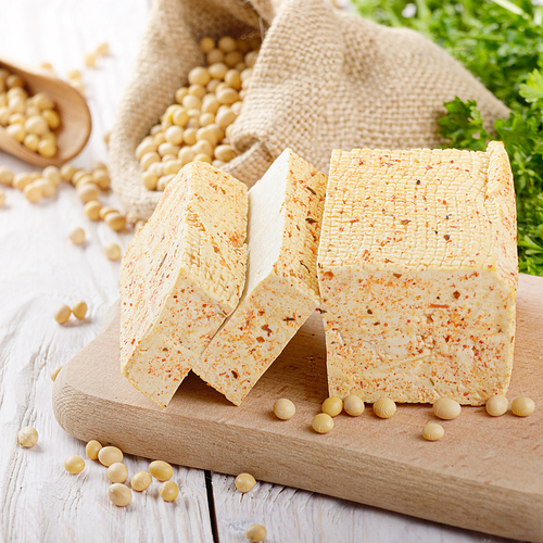 Soy Bean curd tofu on cutting board and in hemp sack on white wooden kitchen table. Non-dairy alternative substitute for cheese