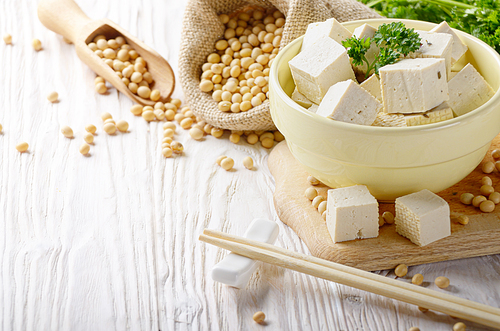 Soy Bean curd tofu in clay bowl and in hemp sack on white wooden kitchen table. Non-dairy alternative substitute for cheese. Place for text