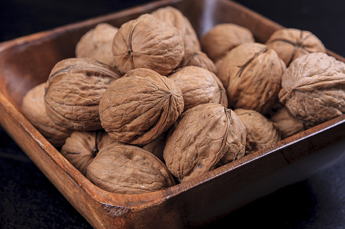 A close up photo of unshelled walnuts in a wooden bowl.