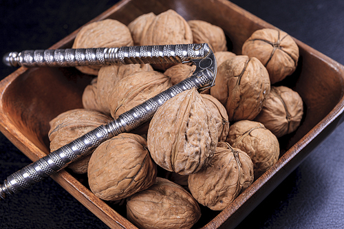 A close up photo of unshelled walnuts and a nutcracker in a wooden bowl.
