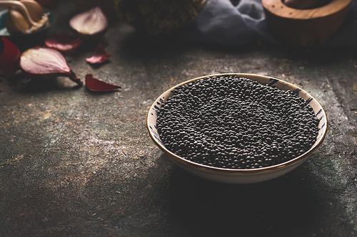 Bowl with black lentil standing on dark rustic kitchen table background with ingredients. Close up. Copy space. Healthy food. Protein rich vegan foods. Plant based protein  source