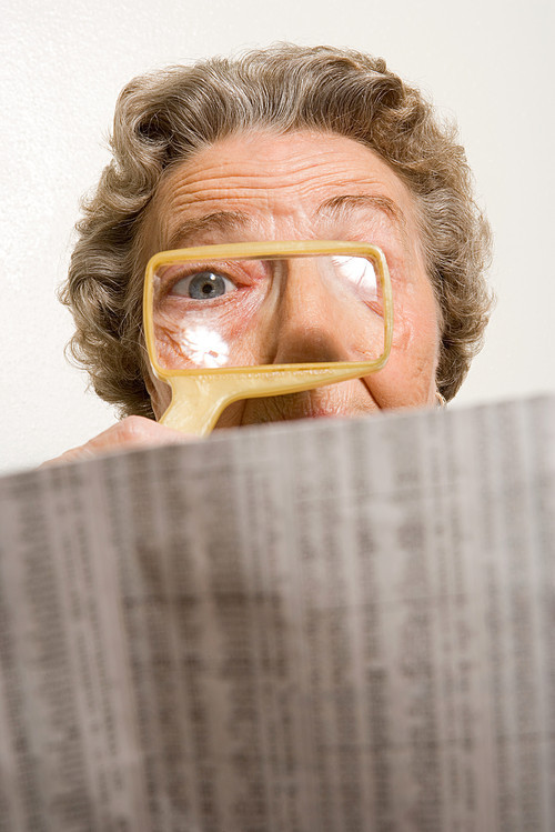 Woman reading newspaper with magnifying glass