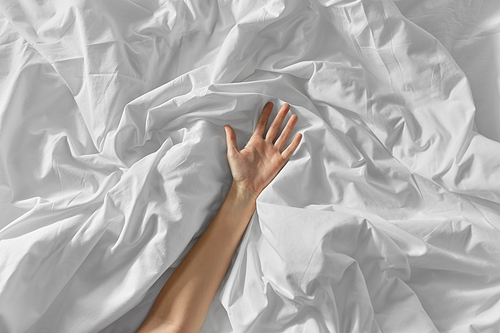 bedtime, sex and rest concept - hand of woman lying on rumpled bed sheet