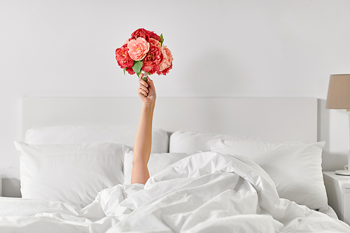international women's day, comfort and morning concept - hand of young woman lying in bed with bunch of flowers at bedroom