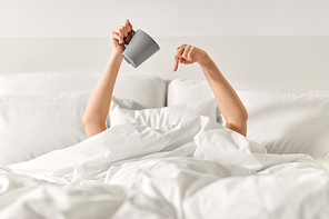 morning, comfort and people concept - young woman with cup of coffee lying in bed at home bedroom
