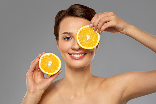 beauty, skin care and detox concept - beautiful woman making eye mask of orange slices over grey background