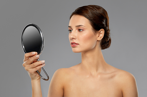 beauty, bodycare and people concept - beautiful young woman with bare shoulders looking to mirror over grey background