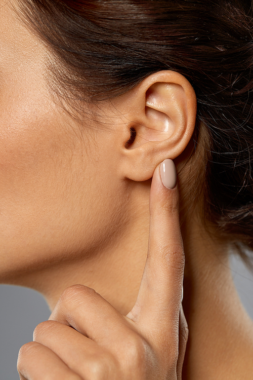 hearing, people and beauty concept - close up of young woman pointing finger to her ear over grey background