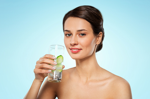 beauty and detox concept - woman drinking fresh water with cucumber and ice over blue background