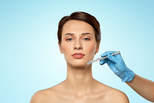 plastic surgery and beauty concept - beautiful young woman and hand with scalpel over blue background