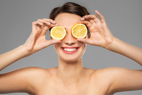 beauty, skin care and detox concept - beautiful woman making eye mask of lemon slices over grey background