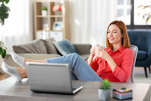 remote job, technology and people concept - happy smiling young woman with laptop computer and coffee having video call at home office with feet on table