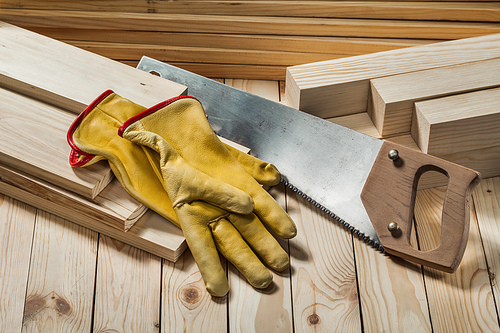 construction gloves and handsaw on wooden background