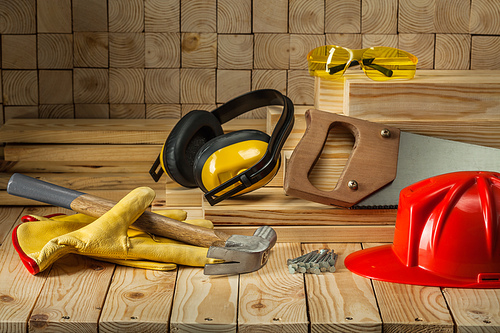 carpentry tools goves helmet goggles hammer handsaw earphones nails handsaw on wooden background