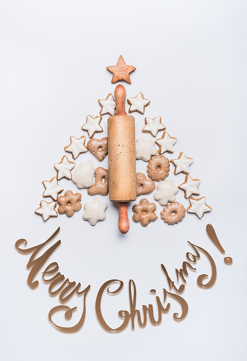 Merry Christmas lettering ,holiday tree made with rolling pin, cookies and gingerbread on white background, top view. Festive layout or pattern for greeting card