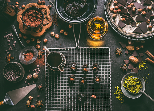 Homemade chocolate pralines preparation on dark rustic table background with vintage kitchen utensils and ingredients. Prunes stuffed with nuts and melting chocolate, top view