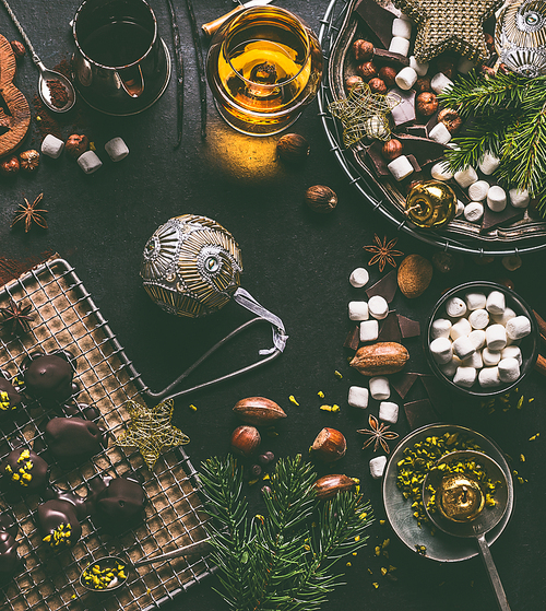 Christmas food background with chocolate, marshmallow, cookies, homemade pralines , cacao , nuts and spirits on dark rustic table with vintage kitchen utensils and ingredients, top view