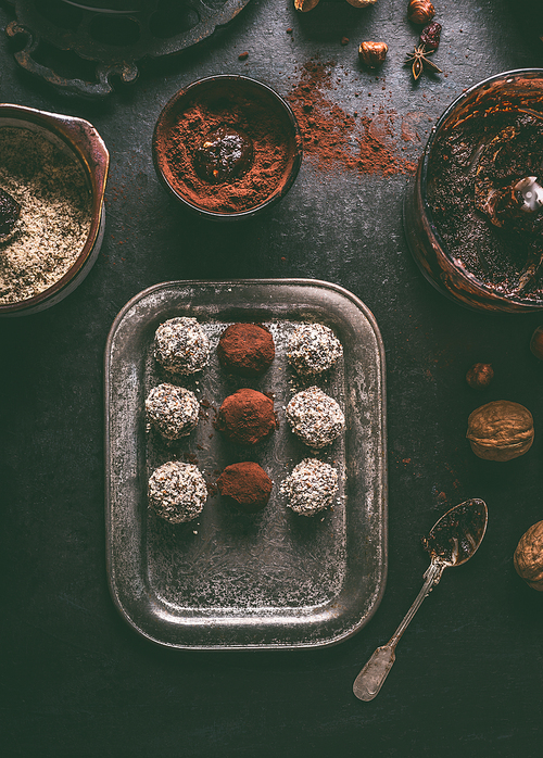 Healthy vegan homemade truffles making. Coated in cacao powder and almond flour truffle balls on dark rustic kitchen table background, top view.