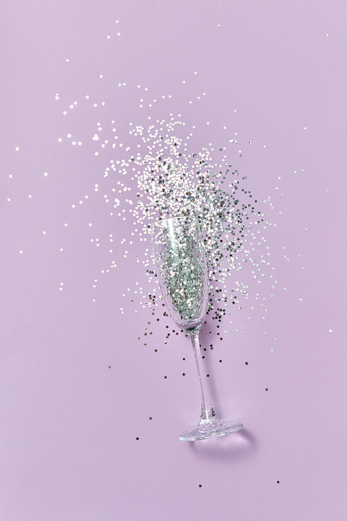 Christmas champagne glass with silver glitter as a alcohol drink bubbles on a pastel lavender background, copy space. Flat lay.