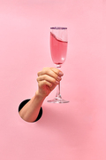Woman hand from the hole holds glass with rose wine on a pastel pink background, copy space. Holiday concept.