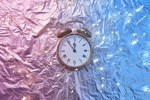 Holiday string of lights and old alarm clock on a duotone pink blue golden background with copy space. Christmas time is at five minutes to midnight.