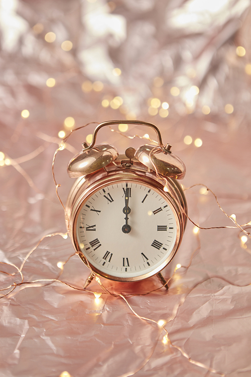 Christmas golden alarm clock on a shiny golden abstract background with copy space. The time is exact midnight. Greeting card.