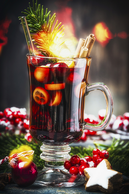 Glass of  traditional mulled wine or punch with Christmas decoration , fir branches and festive bokeh lighting