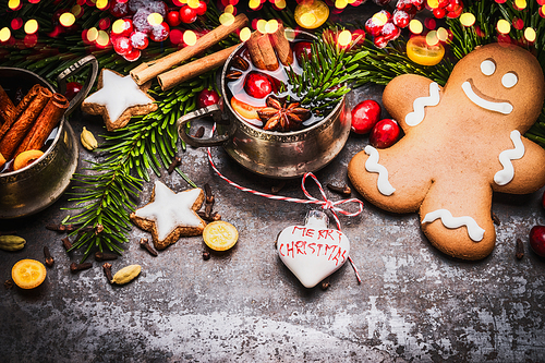 Smiling gingerbread men with mug of mulled wine , Christmas decoration and holiday cookies and spices on dark rustic background with festive bokeh lighting, top view