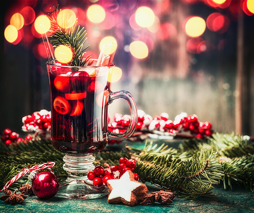 Mulled wine, cookies and holiday decorations on table with bokeh lighting background