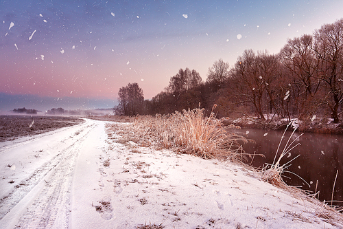 Winter misty dawn on the river. Snowflakes, snowfall. Sunny winter morning. Rural foggy frosty scene