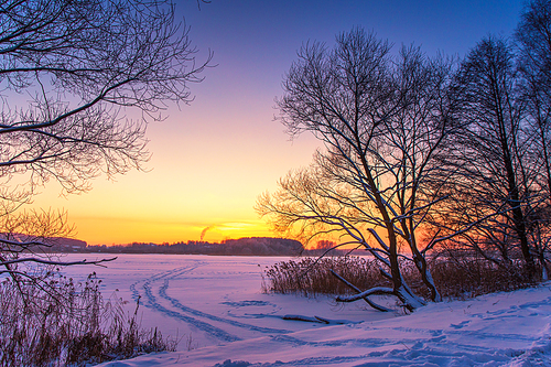 Sunset winter landscape with snow-covered lake in violet and pink colors. Beautiful colorful winter sunset with frozen lake and sunset sky. Winter park. Belarus