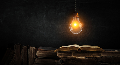 Light bulb on chalk board background and old books