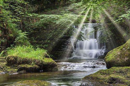 Epic waterfall in forest landscape image with added drama of sun beams breaking through trees in woodland