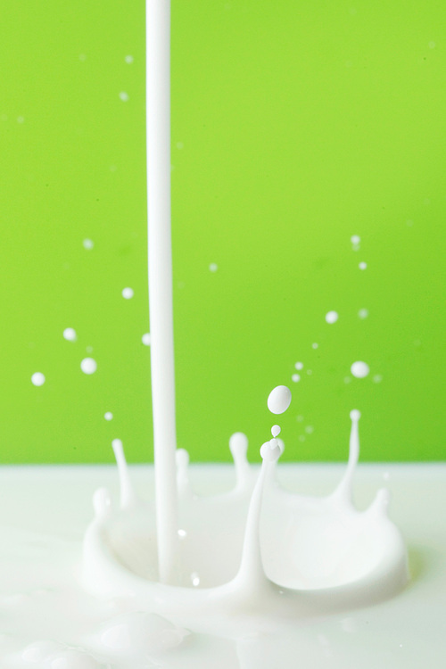 Pouring milk splash on green background close-up