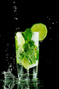 Pouring fresh mojito cocktail in glass notion ice splashing isolated on black background