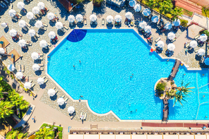 Aerial view of pool, swimming people in transparent blue water, umbrellas, sunbeds, green trees at sunset. Summer holidays. Top view of pool, deck chairs. Relax and leisure in luxury resort in Europe