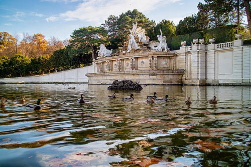 Tranquil fall landscape from monument with ancient statues and pond with floating ducks in a park near Schonbrunn Palace in Vienna, Austria