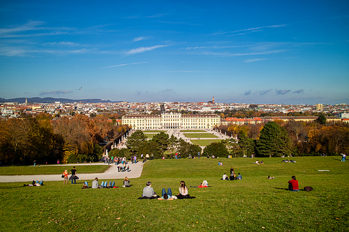 Wonderful landscape with view to Schonbrunn Palace in Vienna, Austria and green wide grass field with sitting and relaxing people on a ground on a blue sky background.