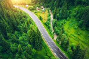 Aerial view of road in beautiful green forest at sunset in summer. Colorful landscape with roadway, pine trees. Carpatian mountains. Top view from drone of highway. View from above. Travel in Ukraine