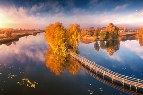 Old fisherman house and wooden pier at sunrise in autumn. Aerial view. Panoramic landscape with house on small island on the lake, colorful trees, jetty, reflection in water. Fall in Ukraine. Top view
