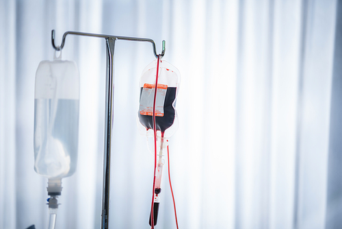 Close-up of Red blood bag and normal saline hanging in hospital ward