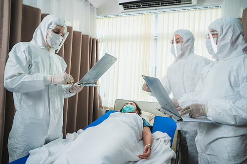 professional doctors in the full protective suits and surgical masks are examining the infected patient in the hospital control area